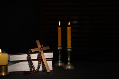 Photo of Church candles, Bible, rosary beads and cross on wooden table, space for text