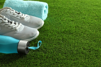 Photo of Bottle of water, sneakers, towel and space for text on artificial grass. Fitness equipment