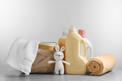 Bottles of laundry detergents, fresh towels, knitted rabbit toy on grey table against white background