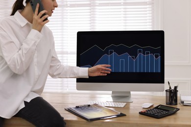 Businesswoman talking on phone while working with computer in office, closeup. Forex trading