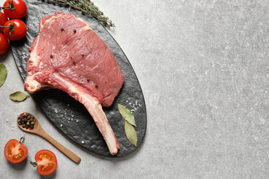 Photo of Raw rib with herbs, spices and tomatoes on grey table, flat lay. Space for text