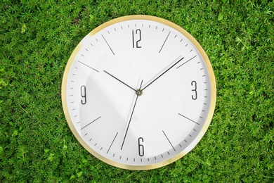 Big clock on green plants, outdoors. Time change concept