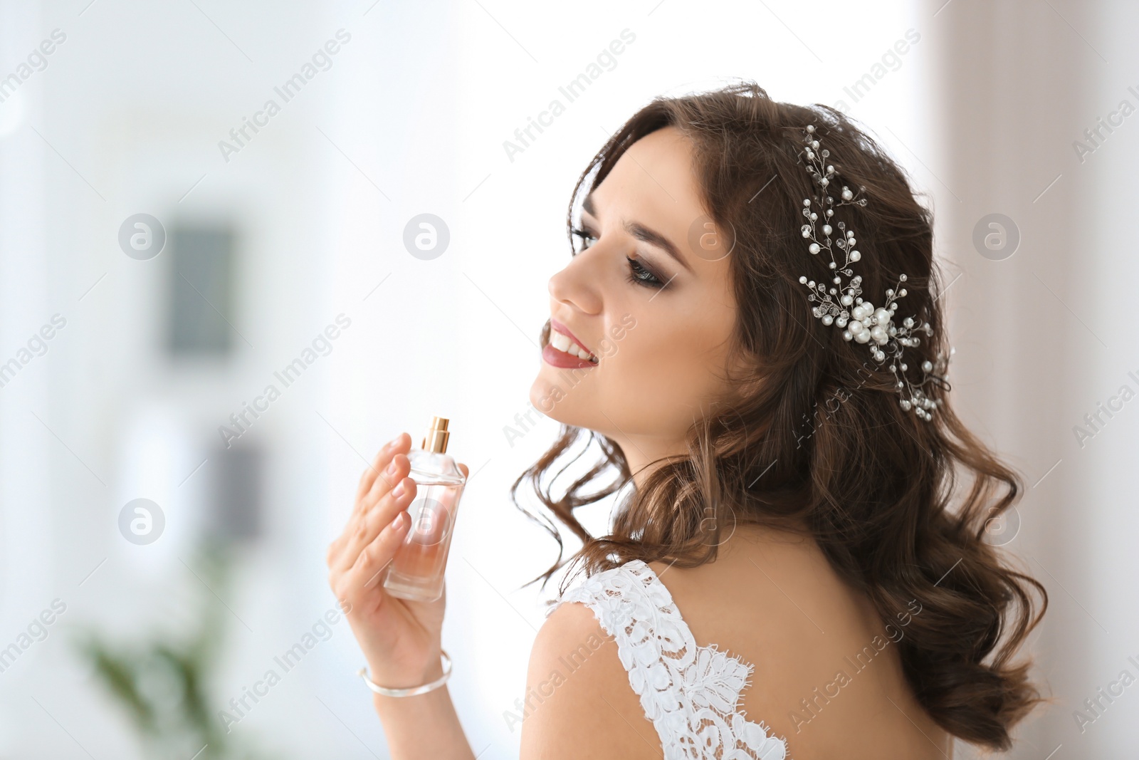 Photo of Beautiful young bride with bottle of perfume on blurred background