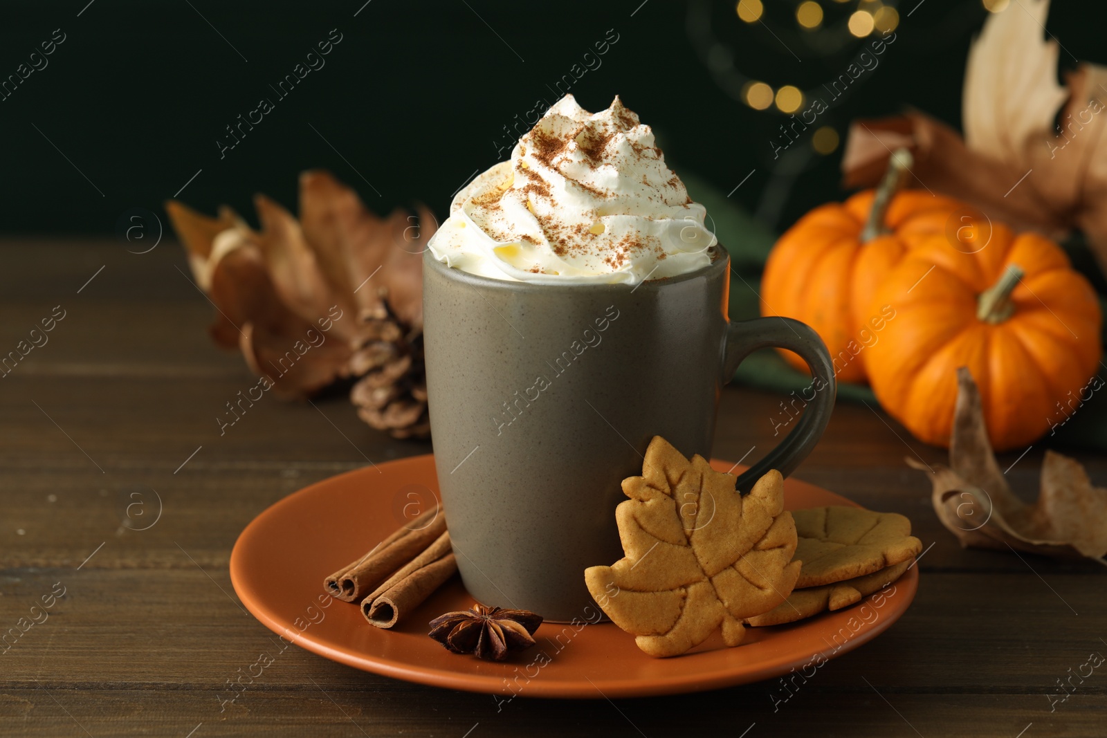 Photo of Tasty pumpkin spice latte with whipped cream in cup and cookies on wooden table, closeup