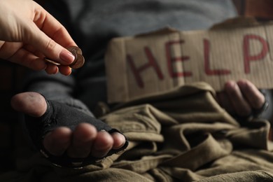 Photo of Woman giving coins to poor homeless man with help sign, closeup. Charity and donation