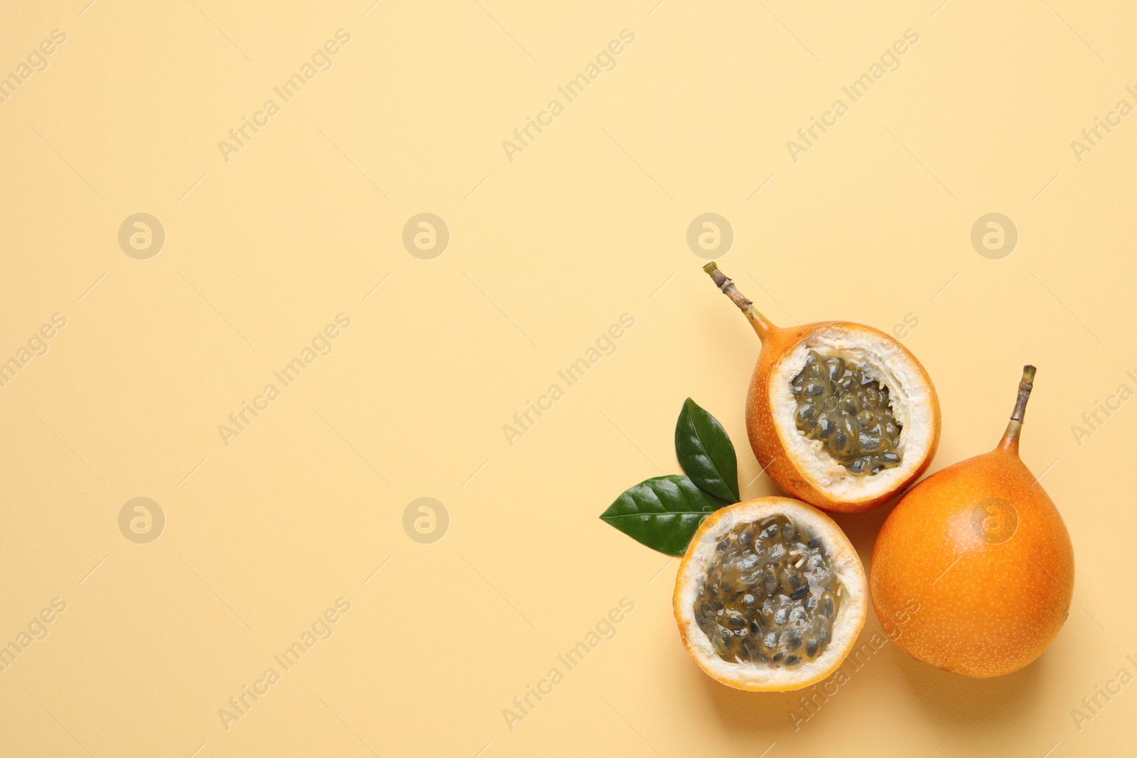 Photo of Delicious ripe granadillas with leaves on beige background, flat lay. Space for text