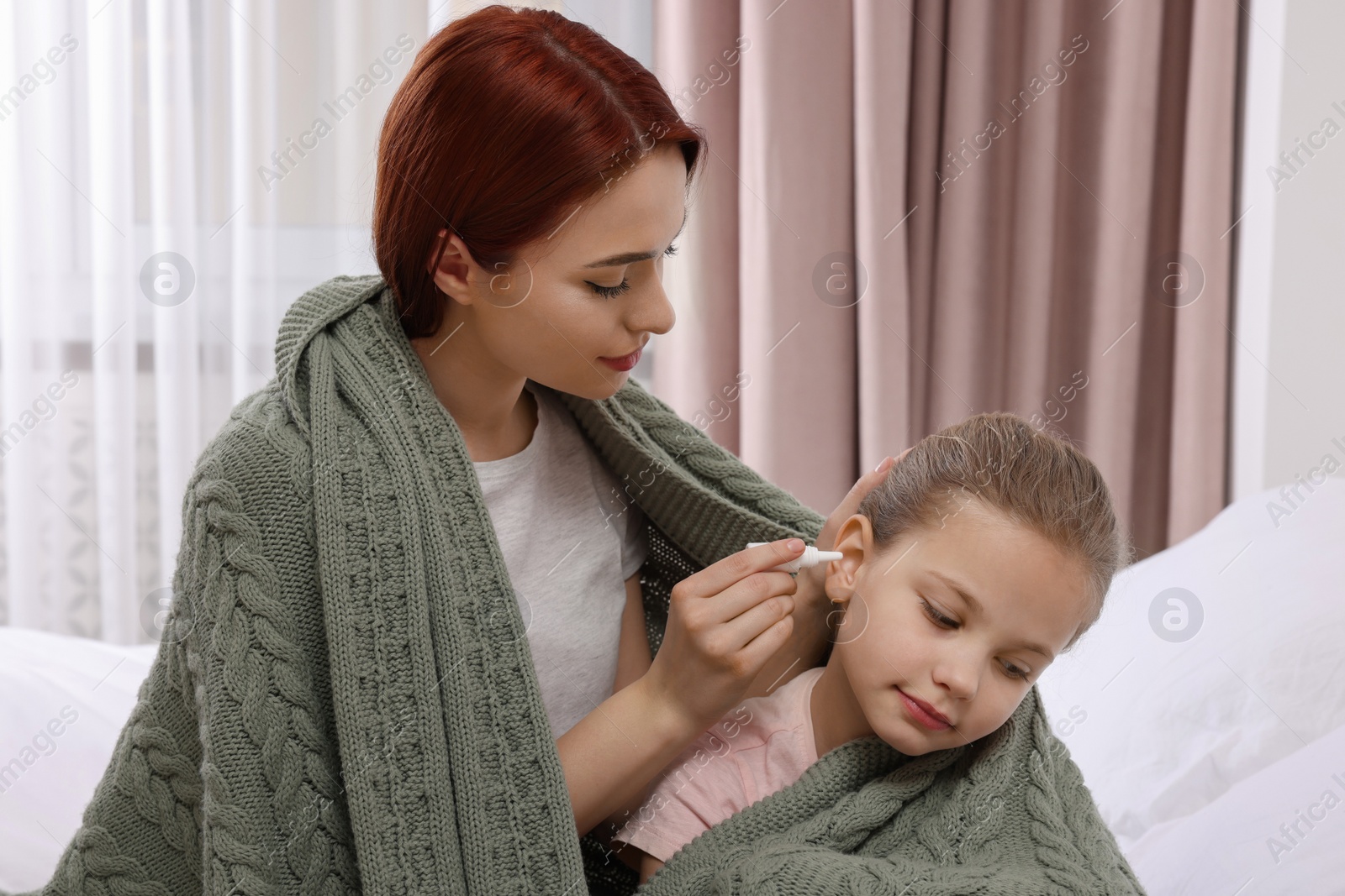 Photo of Mother dripping medication into daughter's ear while being wrapped in warm plaid at home