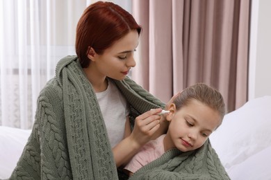 Mother dripping medication into daughter's ear while being wrapped in warm plaid at home