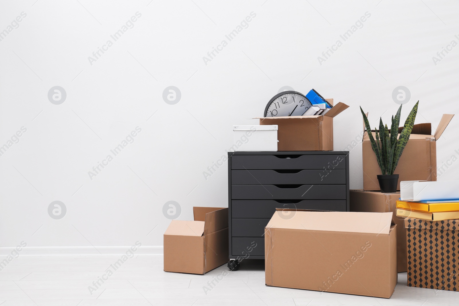 Photo of Cardboard boxes and packed belongings near white wall, space for text. Moving day