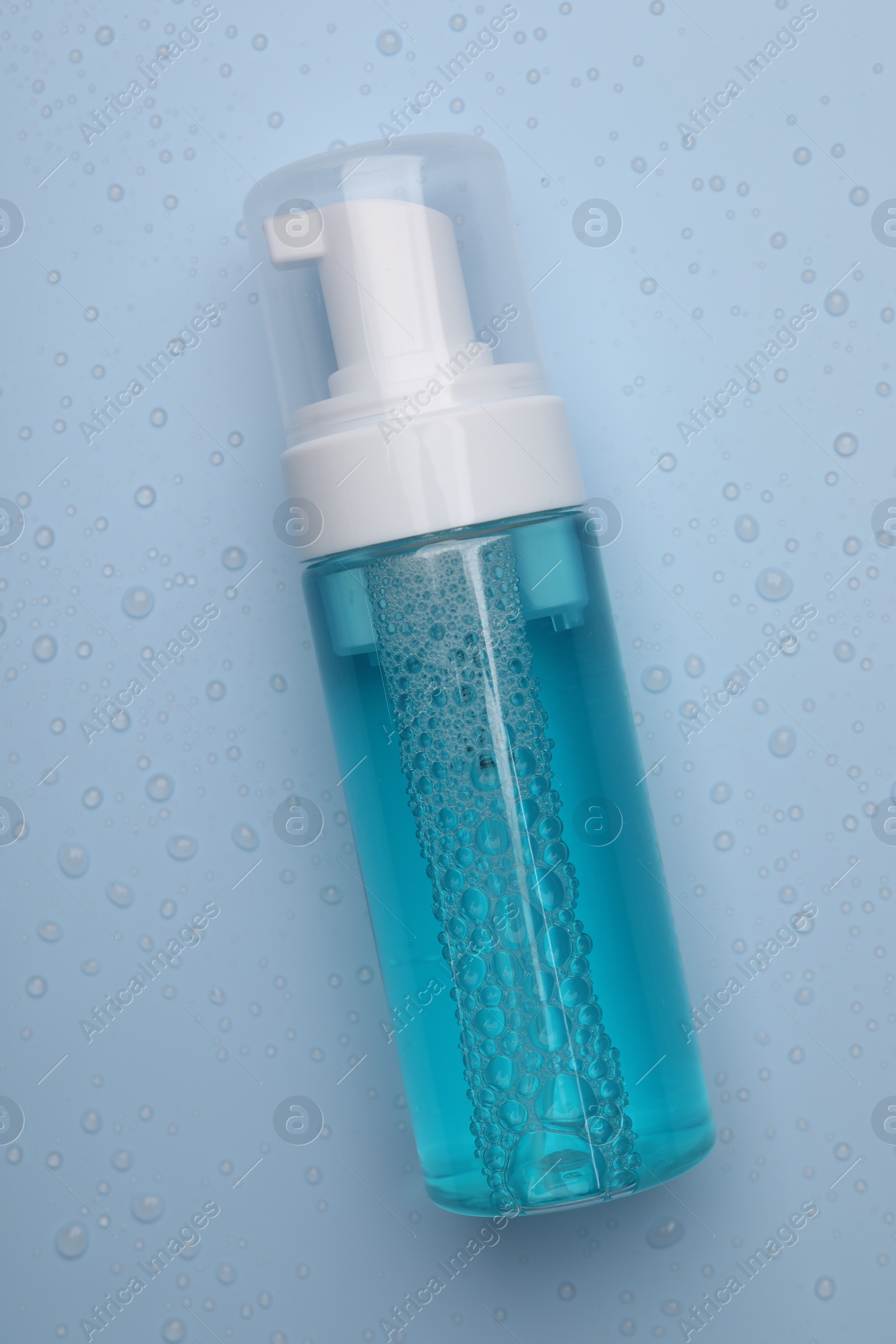 Photo of Wet bottle of face cleansing product on light blue background, top view