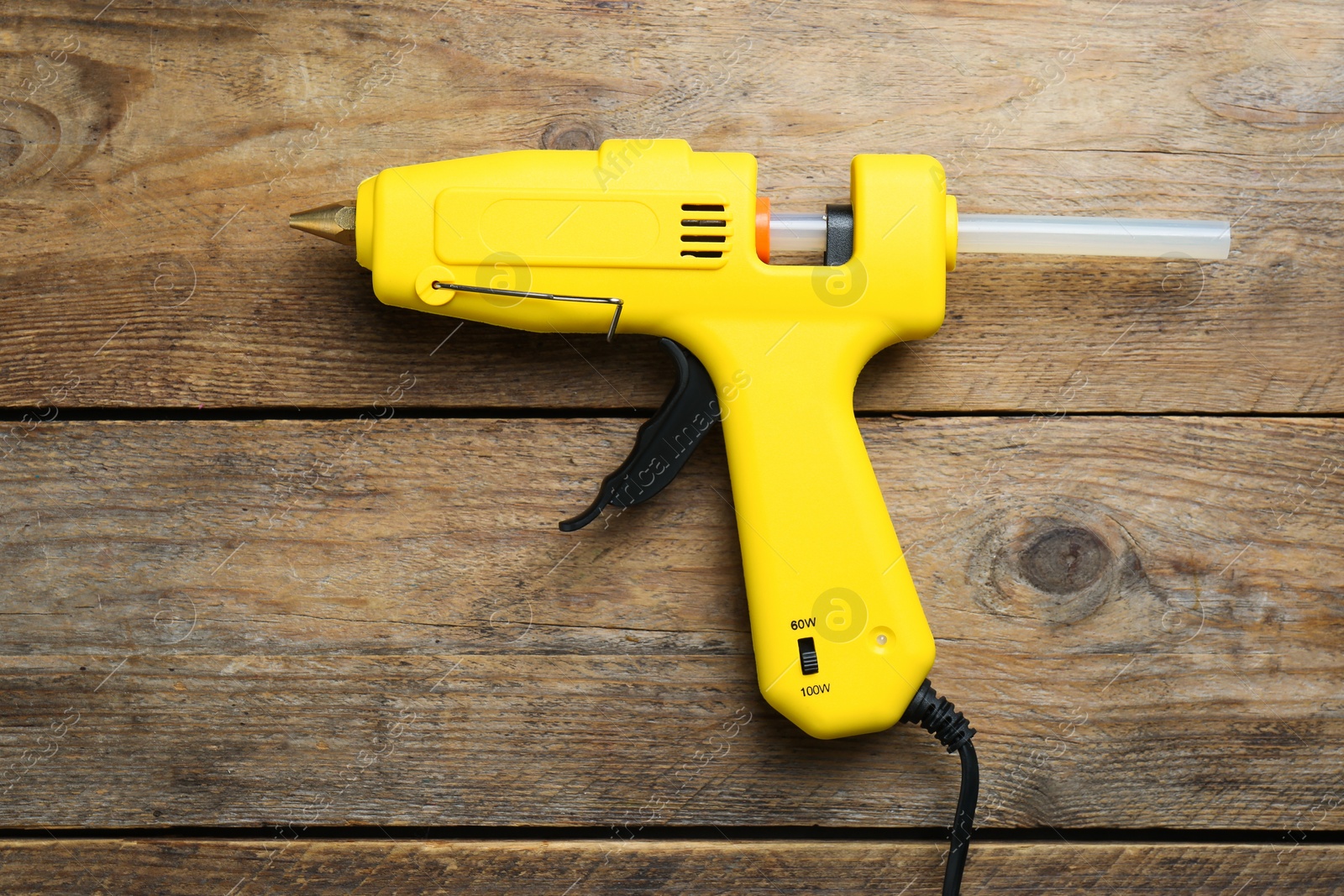 Photo of Yellow glue gun with stick on wooden table, top view