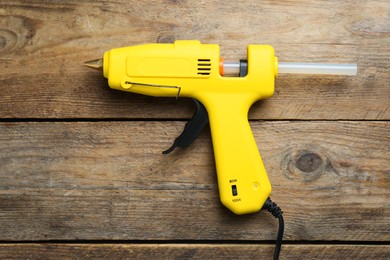 Yellow glue gun with stick on wooden table, top view