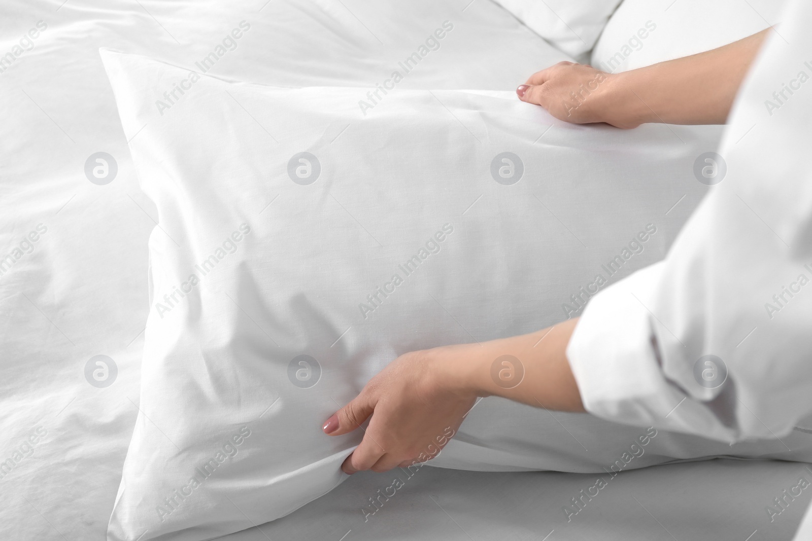 Photo of Woman fluffing soft pillow in bedroom, closeup