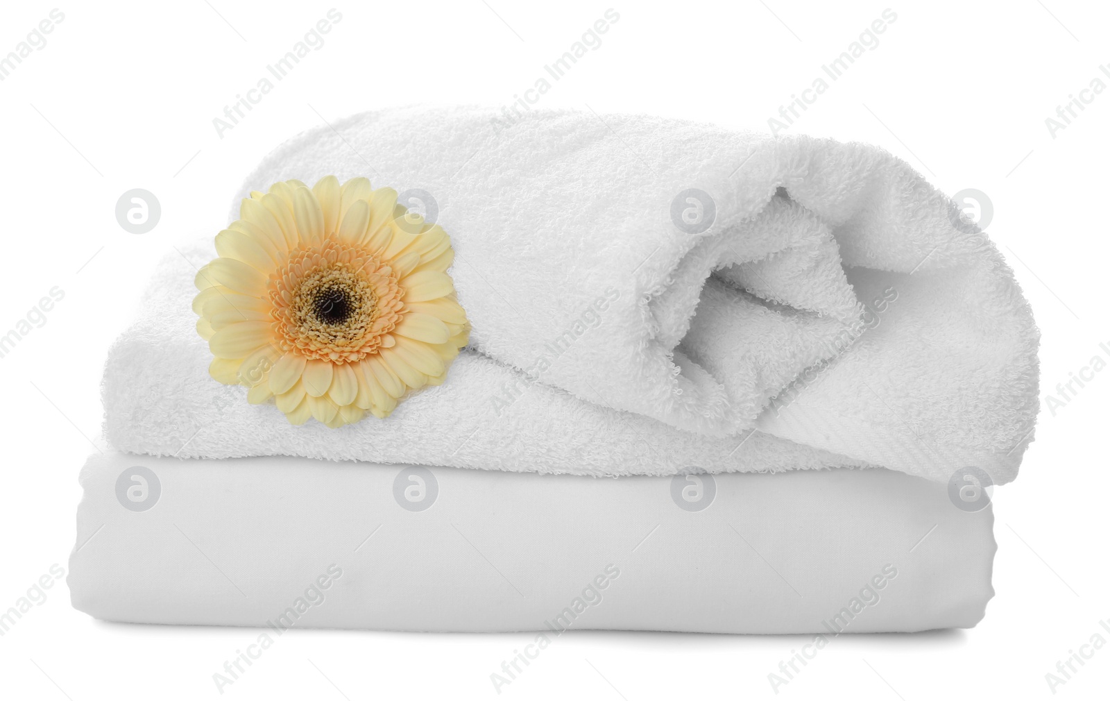 Photo of Fresh clean towels, bed sheet and gerbera on white background