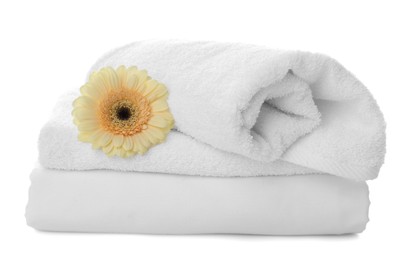 Fresh clean towels, bed sheet and gerbera on white background
