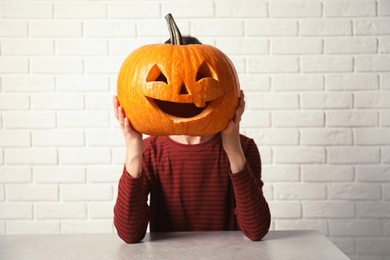 Photo of Woman holding Halloween pumpkin head jack lantern against brick wall