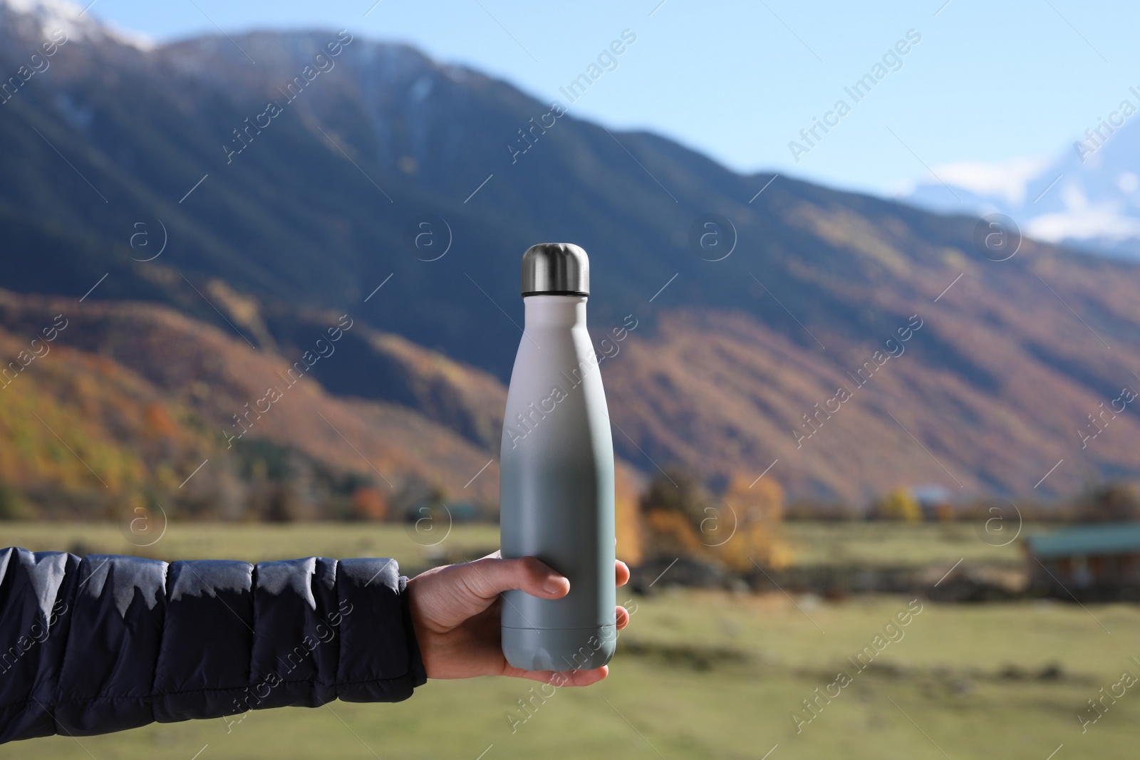 Photo of Boy holding thermo bottle with drink in mountains on sunny day, closeup