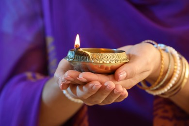 Woman holding lit diya lamp in hands, closeup. Diwali celebration
