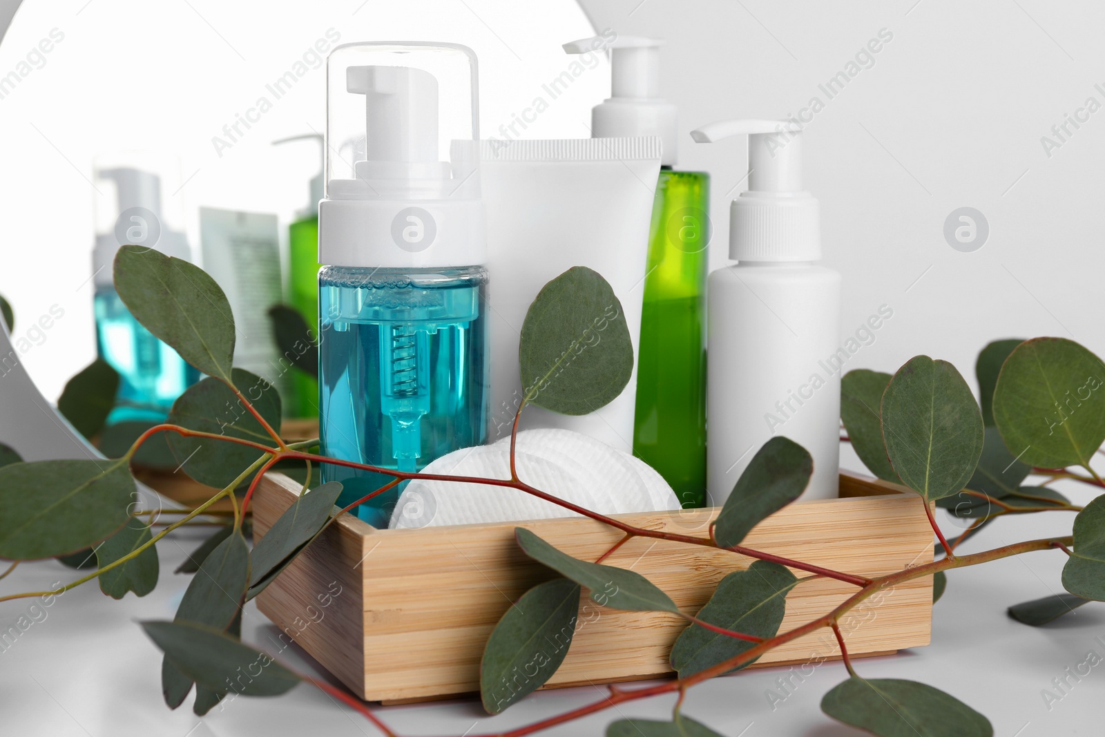 Photo of Different face cleansing products, cotton pads and eucalyptus leaves on white table