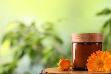 Jar of cosmetic product and beautiful calendula flowers on wooden stump outdoors, space for text