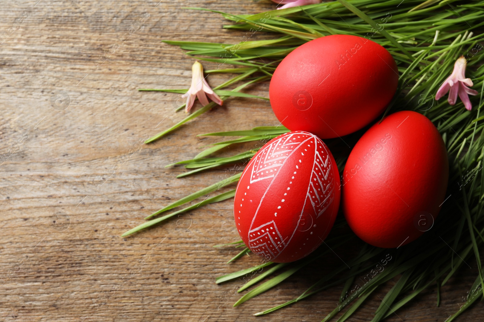 Photo of Flat lay composition of painted red Easter eggs and green grass on wooden table, space for text