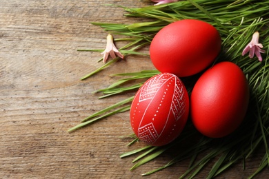 Photo of Flat lay composition of painted red Easter eggs and green grass on wooden table, space for text