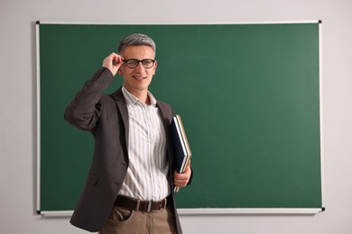 Teacher with notebooks near chalkboard in classroom, space for text