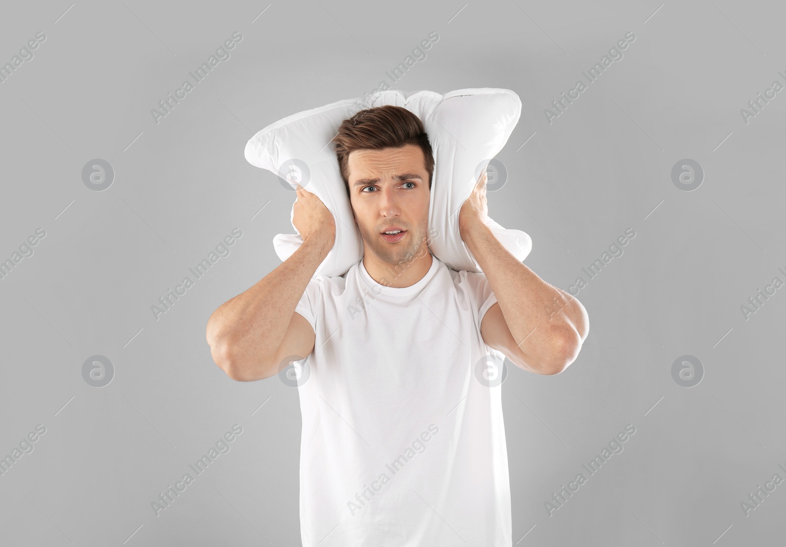 Photo of Young man in pajamas with pillow on gray background