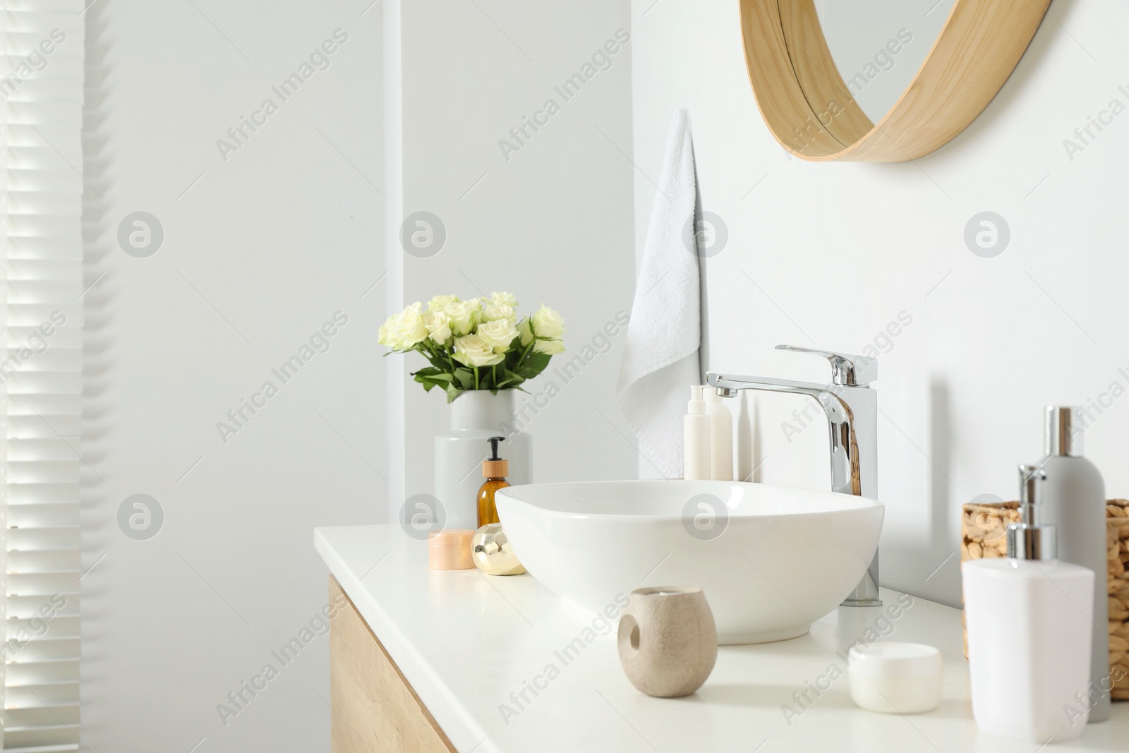 Photo of Vase with beautiful white roses and toiletries near sink in bathroom