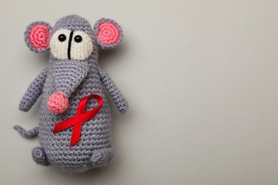Photo of Cute knitted toy mouse with red ribbon on beige background, top view and space for text. AIDS disease awareness