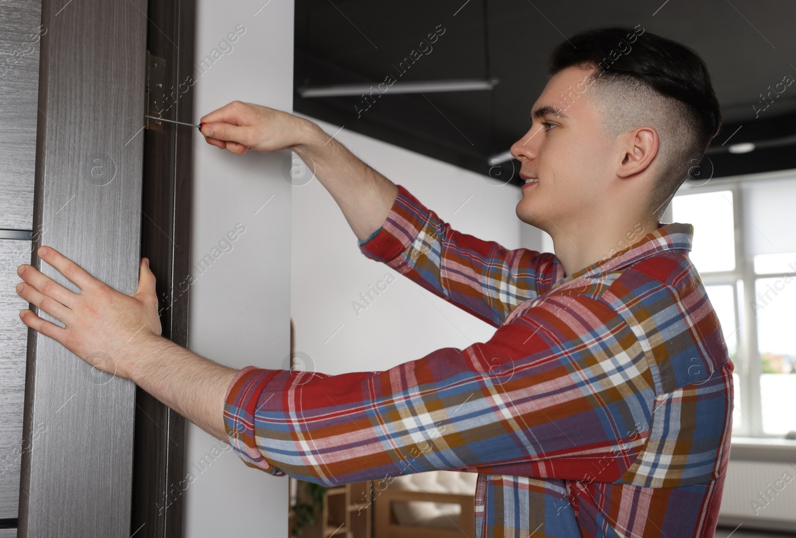 Photo of Young handyman repairing door lock in room