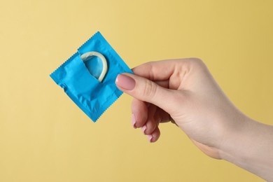 Woman holding condom on pale yellow background, closeup