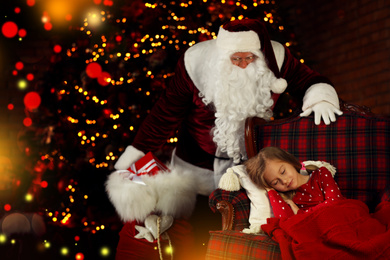 Photo of Santa Claus with Christmas gifts standing near sleeping little girl indoors