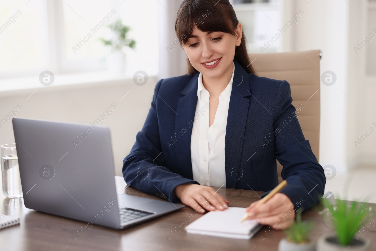 Photo of Woman taking notes during webinar at wooden table indoors