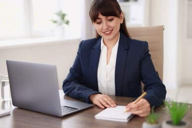 Woman taking notes during webinar at wooden table indoors