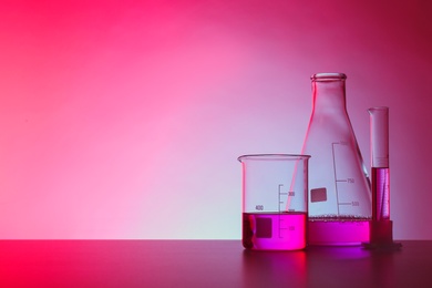 Chemistry laboratory glassware with samples on table against color background