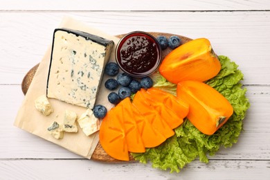 Delicious persimmon, blue cheese, blueberries and jam served on white wooden table, flat lay