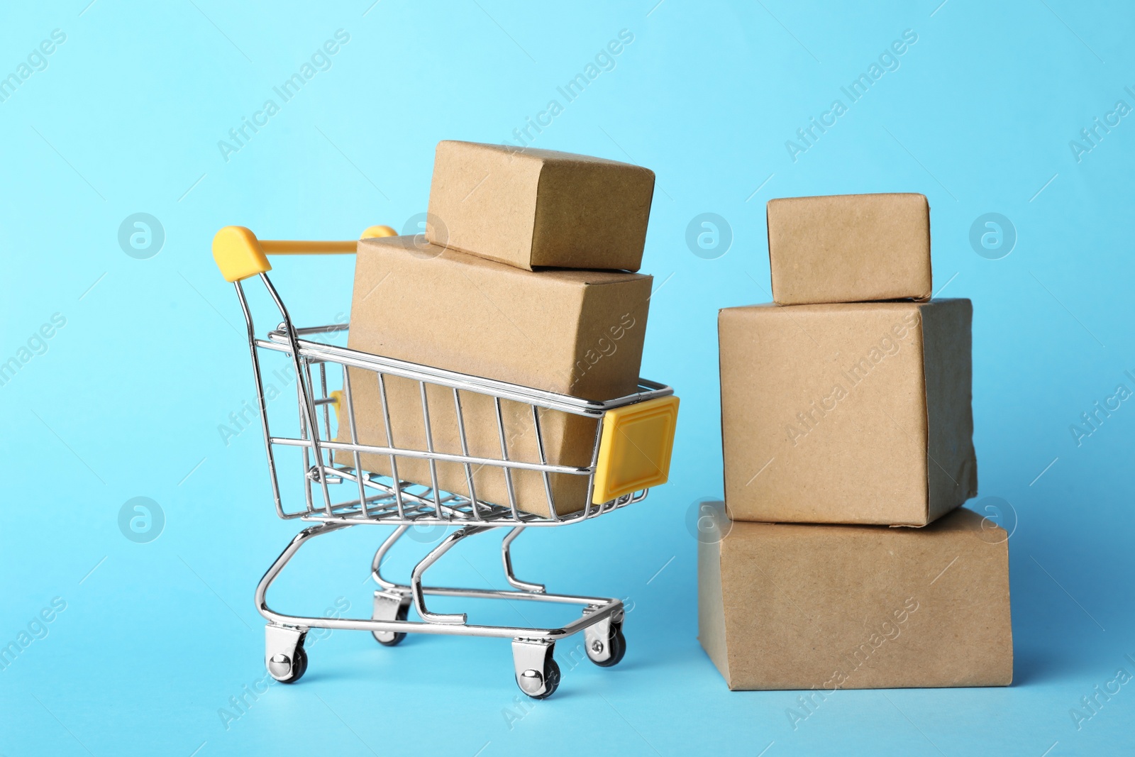 Photo of Shopping cart and boxes on light blue background. Logistics and wholesale concept