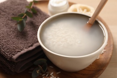 Photo of Bowl with soaked rice and spoon near towel on wooden tray, closeup