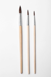 Different paint brushes on white background, top view