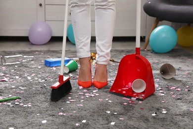 Woman with sweep broom and dust pan cleaning messy room after party, closeup view of legs