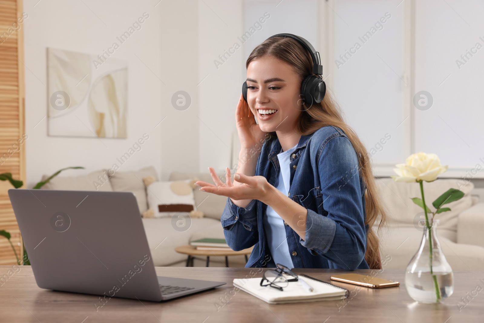 Photo of Happy woman with headphones having video chat via laptop at wooden table