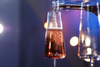 Photo of Rose champagne pouring from bottle into glass on color background, closeup. Space for text