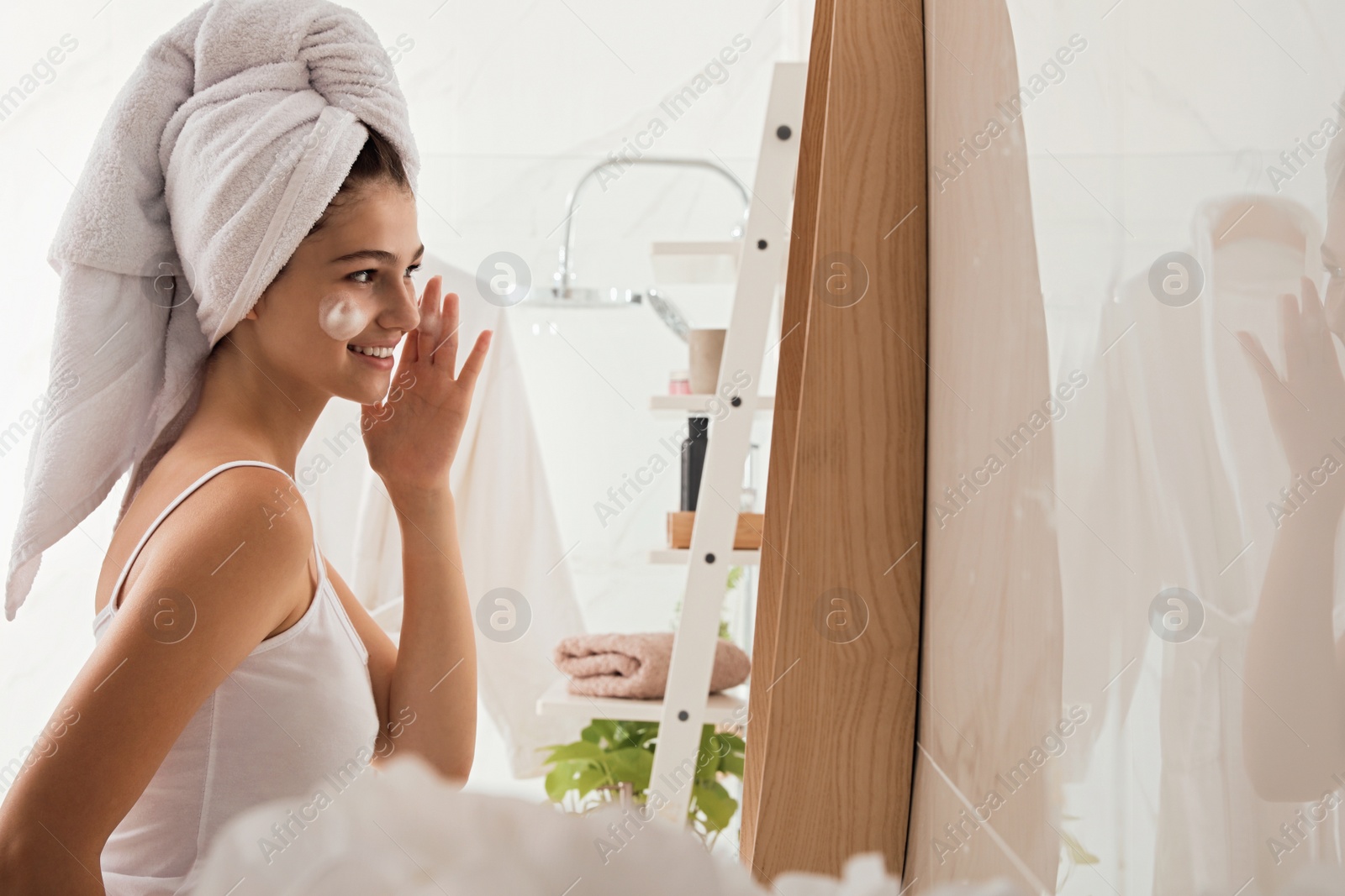 Photo of Beautiful teenage girl washing face with cleansing foam in bathroom. Skin care cosmetic