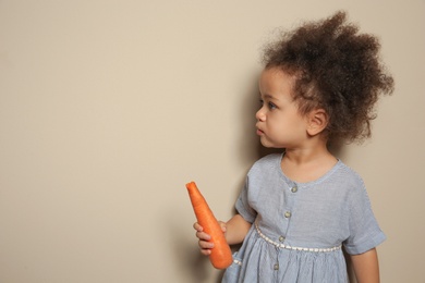 Cute African-American girl with carrot on color background. Space for text