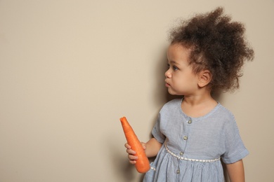 Photo of Cute African-American girl with carrot on color background. Space for text