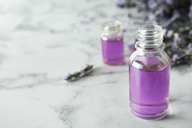 Bottle of natural essential oil and lavender flowers on grey marble background. Space for text