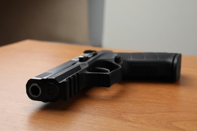 Photo of Semi-automatic pistol on wooden table indoors, closeup. Space for text