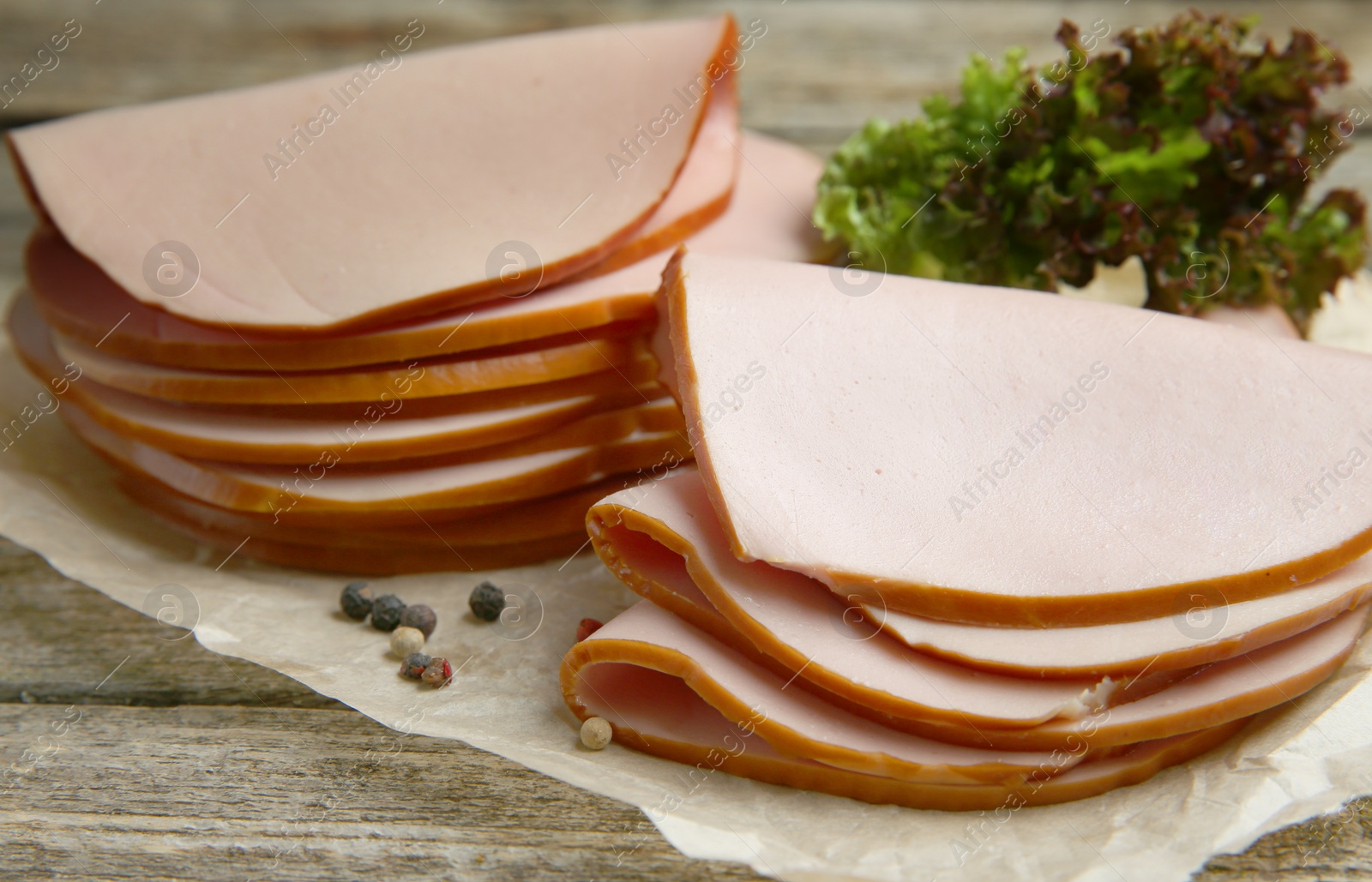 Photo of Slices of delicious boiled sausage with lettuce and spices on wooden table, closeup