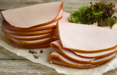 Photo of Slices of delicious boiled sausage with lettuce and spices on wooden table, closeup